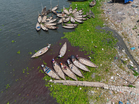 Aerial view of traditional wooden boats on the Buriganga River with green water hyacinths and people on the water in Dhaka, Dhaka Division, Bangladesh.