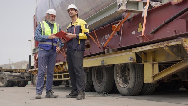 Two engineers collaborate on quality control, inspecting a heavy cargo shipment at an industrial site to manage supply chain logistics and ensure compliance.