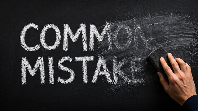 Hand erasing "COMMON MISTAKE" text written in white chalk on a black chalkboard background