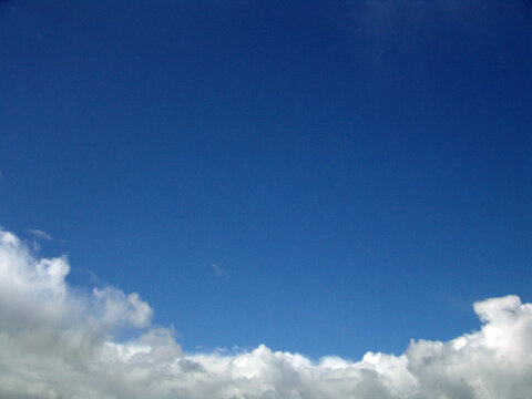 Clear blue sky with soft white clouds gathering along the lower edge, creating a calm, minimalist natural background with ample copy space and a sense of openness.