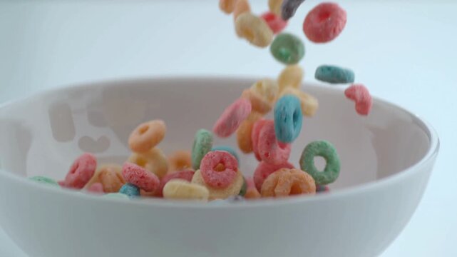 Colorful cereal rings falling into a white bowl on a plain background