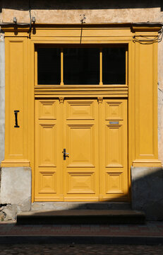 Bright yellow vintage wooden door with decorative panels and transom window on an aged building facade, highlighted by sunlight and shadows.