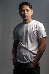 Fototapeta premium An Asian man from Indonesia wearing a white t-shirt stands posing in front of the camera. Isolated against a gray background.