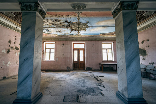 Abandoned palace hall with marble columns, damaged ceiling, peeling walls, neoclassical interior, heritage preservation, renovation project.
