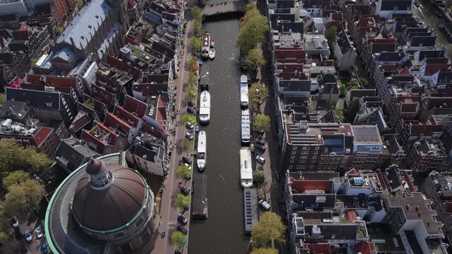 Aerial flight over Ronde Lutherse Kerk church and Amsterdam's city center showing classic dutch architecture, canal houses, historic buildings and tour boats sailing