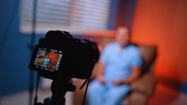 Modern camera directed on the man in chair wearing blue uniform. Close up. Blurred backdrop. Medical blog concept.