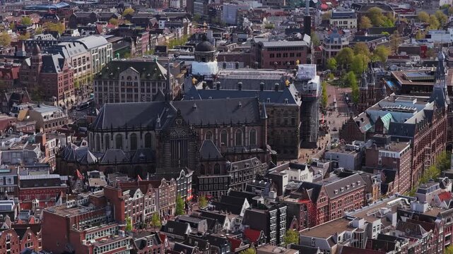 Flying over historic Oude Kerk church and iconic Royal Palace Amsterdam in Netherlands, showing famous european architecture and dutch culture on Dam Square