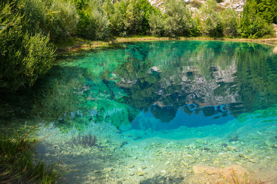 Deep turquoise karst spring with crystal clear water reflecting green vegetation and rocky cliffs