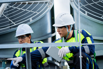 Two engineers in safety gear are conducting a safety check on the roof of an industrial building. Industrial building technicians are working on the roof of a large office building. © KANGWANS