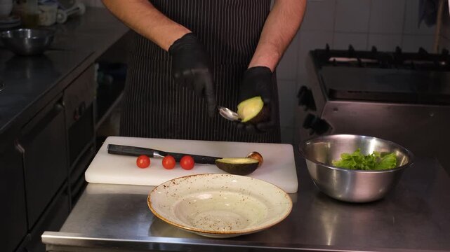 Male chef in restaurant cutting and slicing avocado for salad on kitchen cutting board

