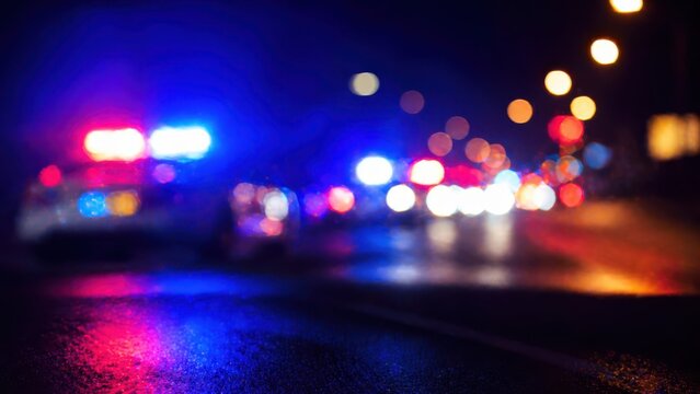 Blurry police car lights at night on wet road abstract background with bokeh effect and red blue reflections.