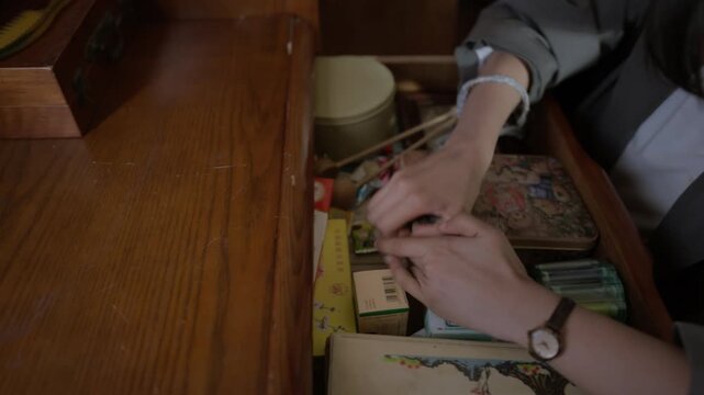 Young asian woman rummaging through a messy drawer, finding old objects and photographs at home