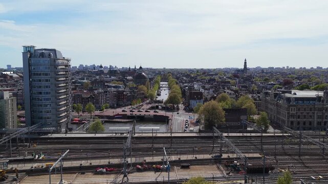 Amsterdam Central Station railway revealing Singel canal with Basilica of Saint Nicholas, historic dutch houses, bustling city street traffic under blue sky