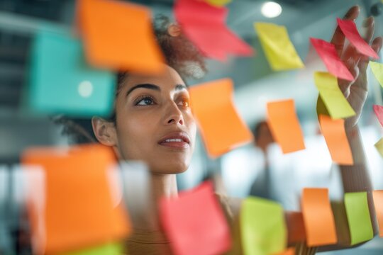 Woman project manager sticking adhesive note on glass wall. Professional worker brainstorming with memo sticker in office. Creative planning, strategy development and agile team concept.