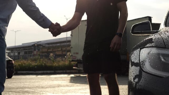 Male arm giving key of car to buyer of modern auto at sunny rainy day. Handshake between salesman and new owner of electric automobile after successful deal. Concept of buy or rent car. Slow motion