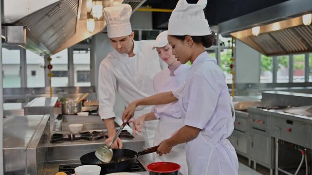 Professional male chef teaching diverse female students how to cook in modern culinary school kitchen
