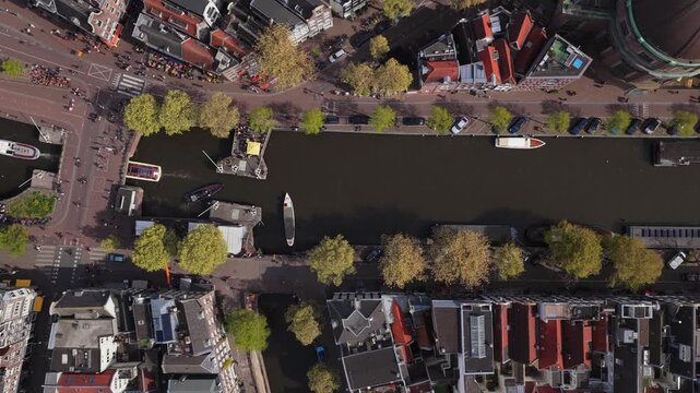Amsterdam top down shot showing boats moving along Singel canal with traditional dutch houses, Koepelkerk church dome, people walking on streets in Netherlands