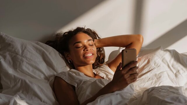 Young woman relaxing in bed while browsing on smartphone  