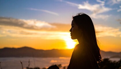 Fototapeta premium A beautiful young woman silhouette looking at the golden sunrise over mountains and clouds representing peace and mindfulness lifestyle.