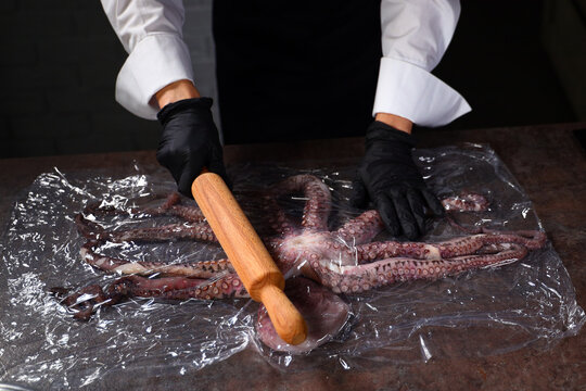 Cook chops octopus with wooden rolling pin before cooking dish. Octopus is wrapped in plastic wrap. Protein food. Seafood dishes.