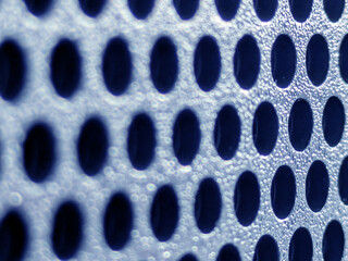 Obraz premium Close-up of shiny perforated metal surface with blurred background and patterned holes