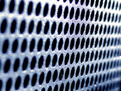 Close-up of shiny perforated metal surface with blurred background and patterned holes