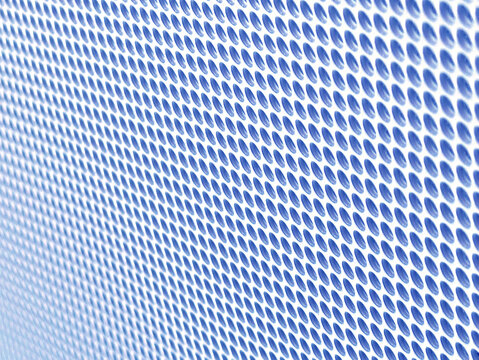Close-up of shiny perforated metal surface with blurred background and patterned holes