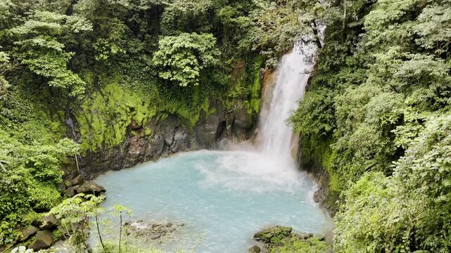 Turquoise waters churn at base of towering jungle waterfall framed by lush emerald cliffs and dense rainforest canopy