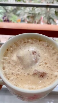 Morning hot espresso coffee or Americano in a black glass cup. Beautiful black cup of black coffee. Art and presentation of delicious hot coffee. Coffee art on a cappuccino. hand presenting a small bl