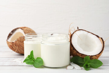 Obraz premium Delicious coconut yogurt in glass jars, mint leaves and fruits on white wooden table, closeup