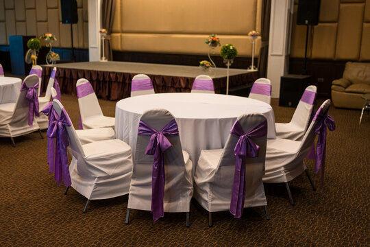 Wedding chairs with purple bow with stage. Elegant white chair covers