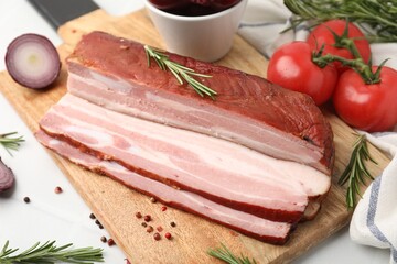 Fototapeta premium Pieces of smoked bacon with peppercorns, rosemary, onion and tomatoes on white table, closeup