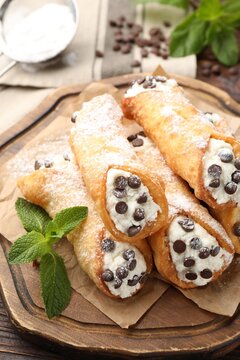 Delicious cannoli with cheese, chocolate chips, powdered sugar and mint on wooden table, closeup