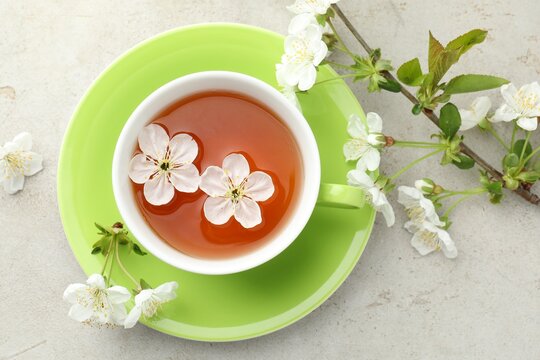 Aromatic tea in cup and flowers on light grey table, flat lay