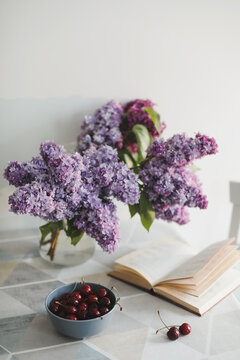 Romantic still life with an open book, lilac flowers and cherries on a table 