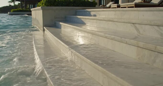 Water waves splashing over white marble swimming pool steps at sunset