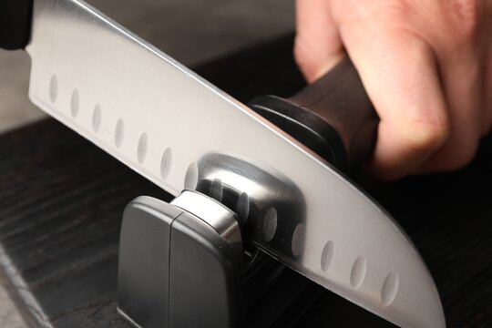 Man sharpening knife at grey table, closeup
