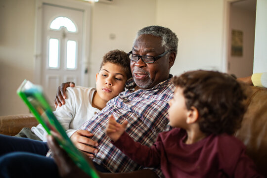 Grandfather reading a story to grandchildren on the sofa at home