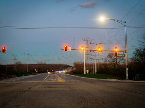 A street view of a multi lane road intersection at dusk in Naperville Illinois with multiple red traffic lights glowing and power lines against the sky
