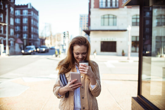 Young woman texting and drinking coffee on city street