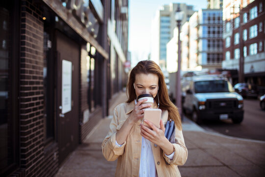 Woman drinking coffee and using smartphone on city sidewalk
