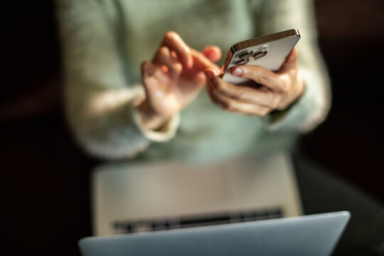Person using smartphone while working on laptop at home