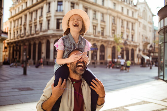 Father giving laughing daughter a shoulder ride on historic city street