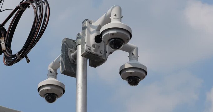 Low-angle shot of security camera array featuring three white dome CCTV units mounted on metal pole. Strategic positioning provides 360-degree surveillance coverage for comprehensive urban monitoring