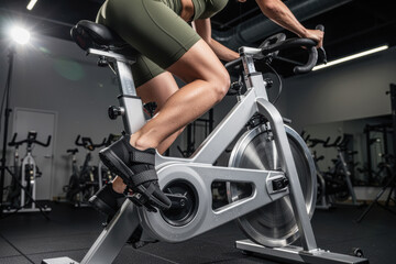 Fototapeta premium Woman on stationary bike pedaling in gym with focus on lower body strength