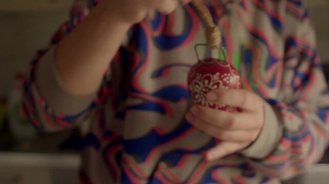 hands holding red decorative ornament with white floral pattern colorful shirt backdrop, delicate inspection and gentle handling, cozy festive mood in kitchen craft scene