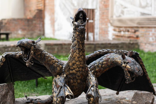 Close-up of a three-headed dragon statue with wings and scaled metal texture outdoors. Fantasy sculpture with medieval character, ideal for mythology, heritage, and design themes.