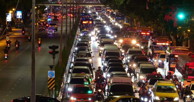 Nighttime view of congested arterial road in Bangkok, with countless cars, motorcycles, and buses in congestion at ongoing lanes, outgoing lanes are empty