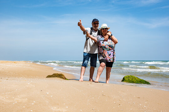 Pareja de jubilados en la playa saludando con los pulgares hacia arriba.