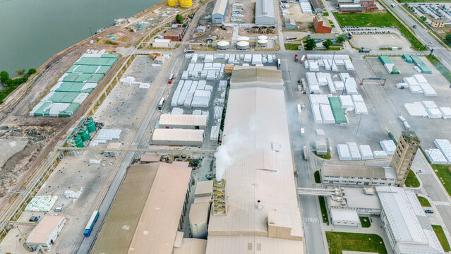 Aerial view of an industrial complex with large warehouses, stacks of materials, and a smoking chimney in Sabac, Vojvodina, Serbia.